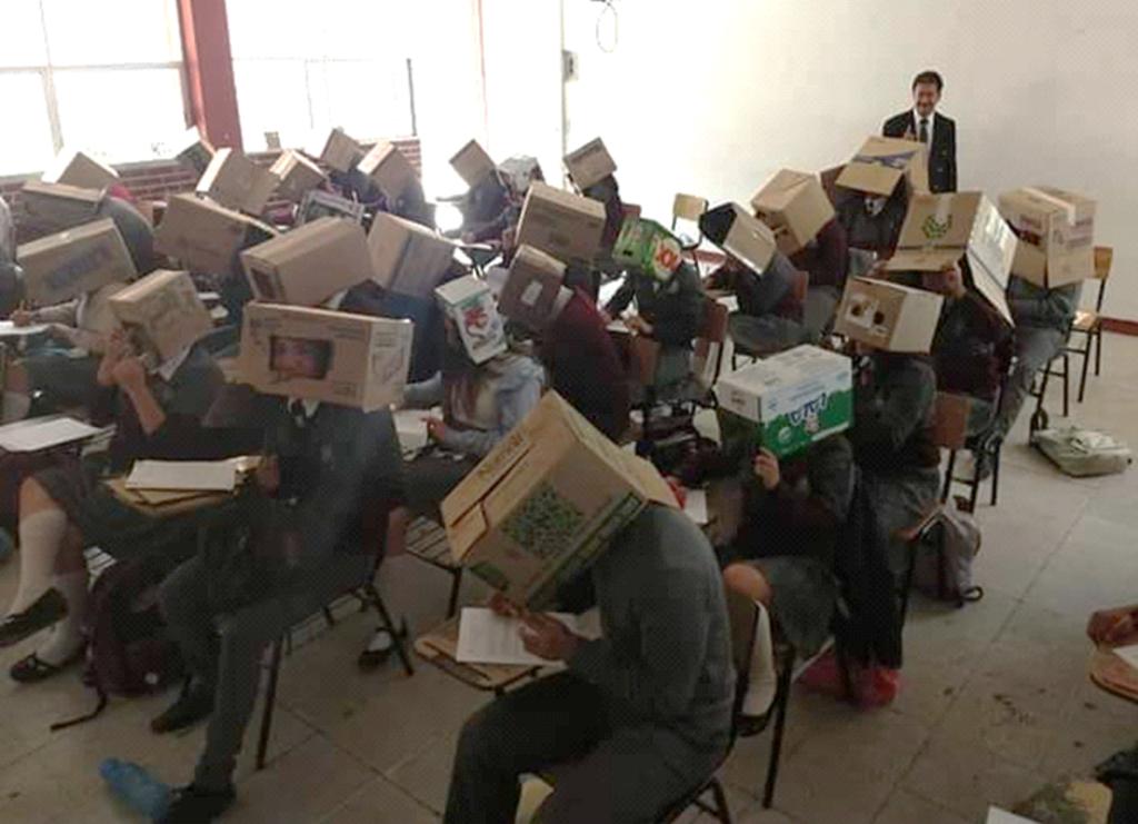 Profesor coloca cajas de cartón en las cabezas de sus alumnos